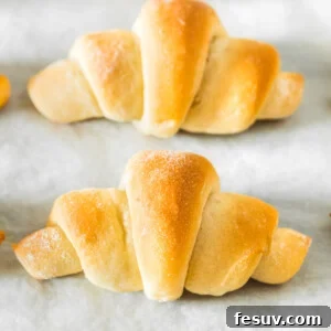 A row of crescent rolls on a parchment-lined baking sheet, golden and ready to be served.