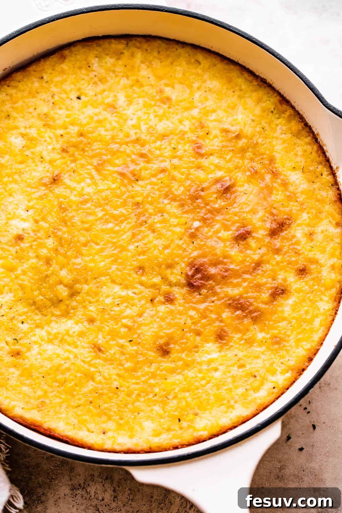Golden brown baked corn pudding in a large white cast iron skillet, ready to be served.