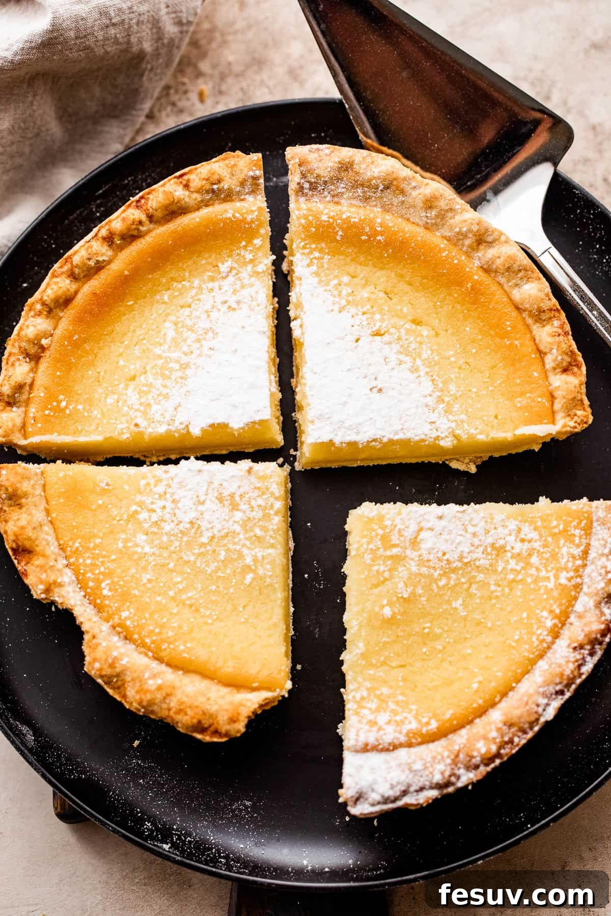 overhead shot of black plate with buttermilk pie cut into 4 slices and dusted with powdered sugar.