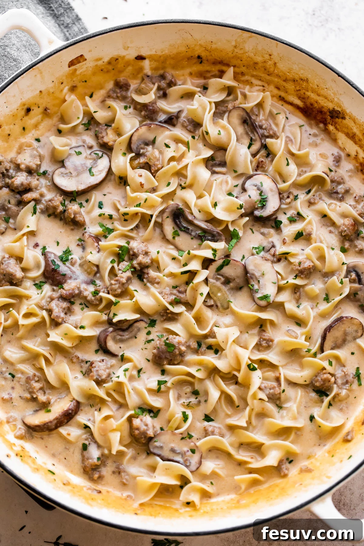 overhead shot of a white braiser filled with cream sauce, noodles, mushrooms, and beef.