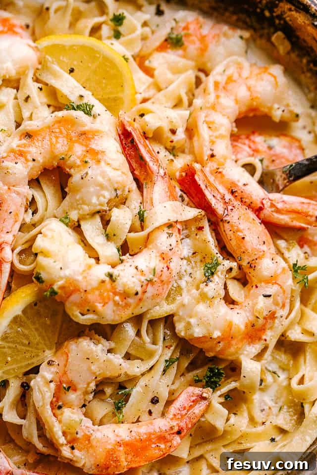 Rich & Decadent Shrimp Alfredo: Ready in Minutes Close up of Creamy Shrimp Alfredo Pasta in a pan garnished with lemon wedges.