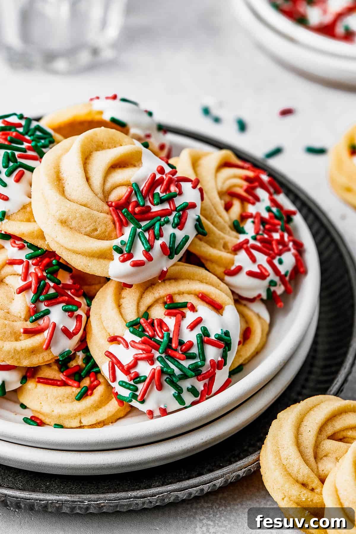 A small dessert plate stacked on top of several other plates, and piled with iced butter cookies.