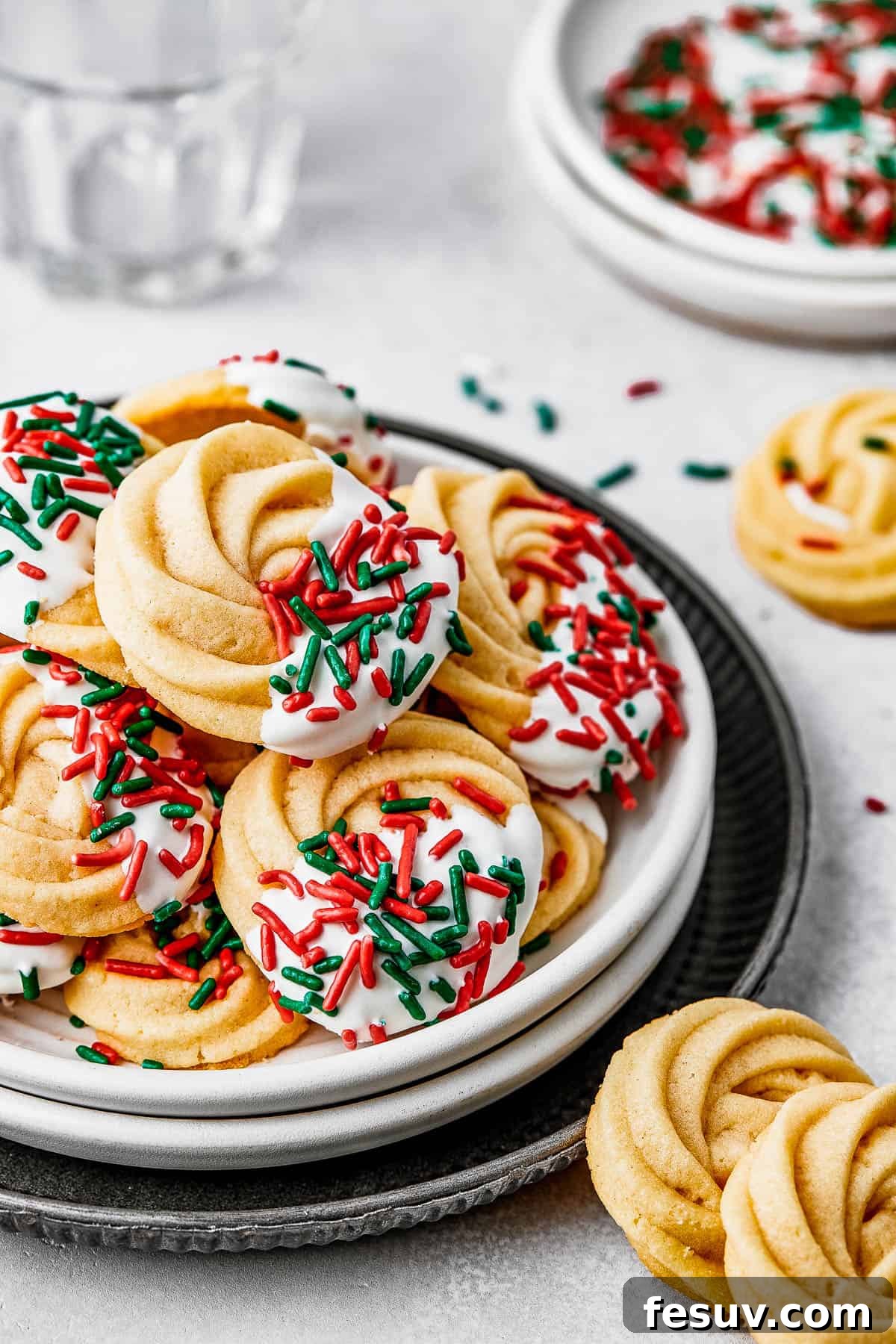 A small dessert plate stacked on top of several other plates, and piled with iced butter cookies.