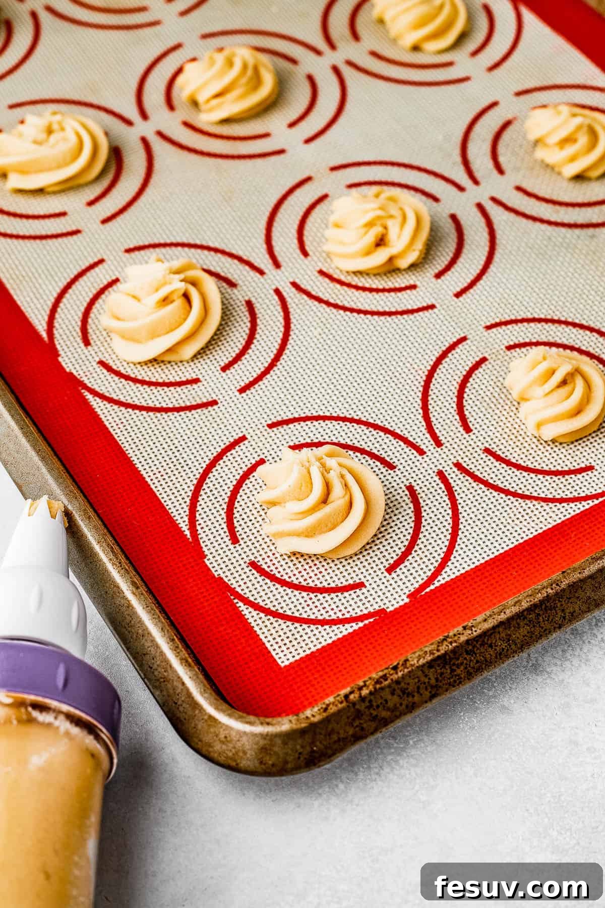 Unbaked butter cookies, piped onto a silicone baking mat on a large cookie sheet.