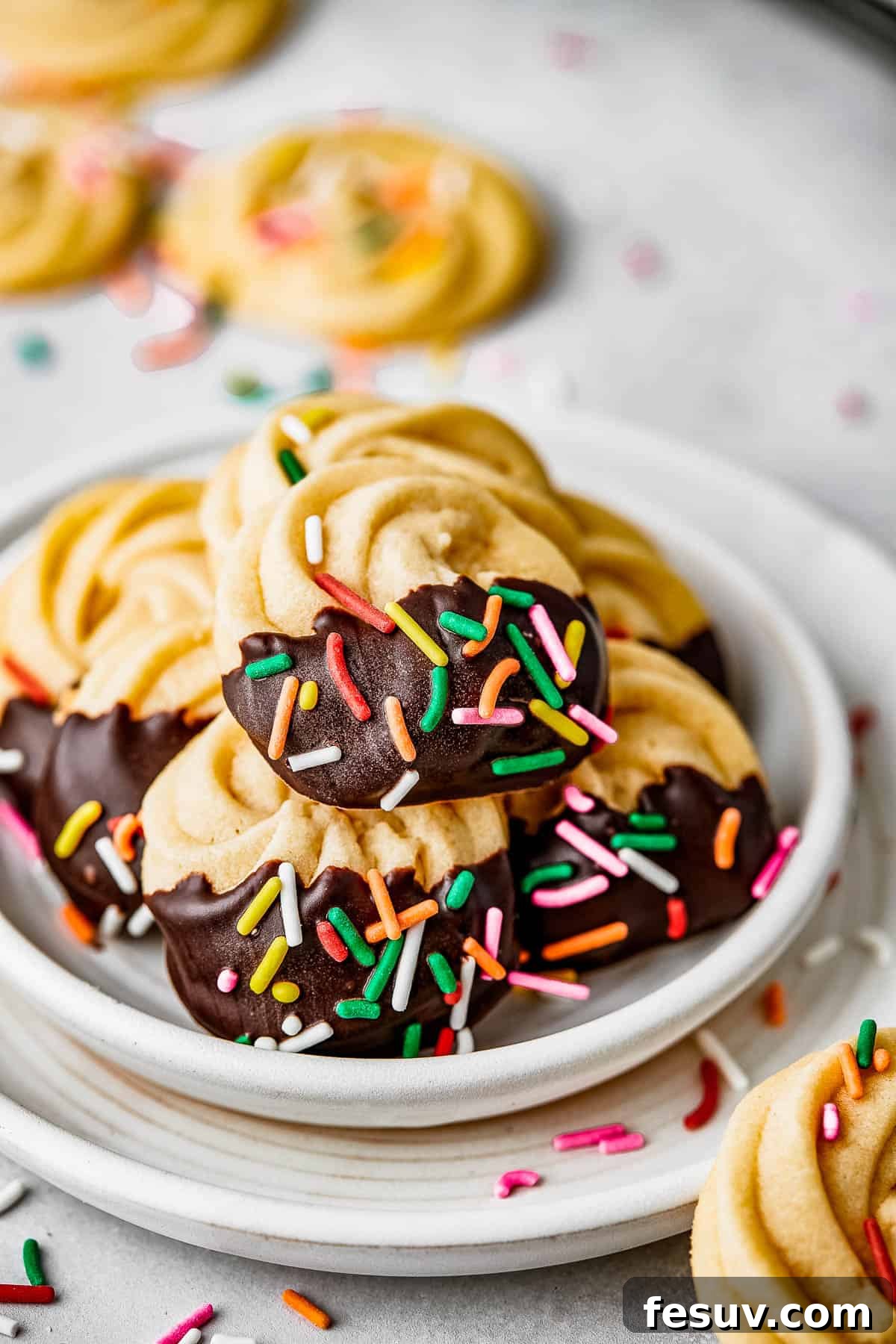 Chocolate iced butter cookies with multicolor sprinkles on a white plate.