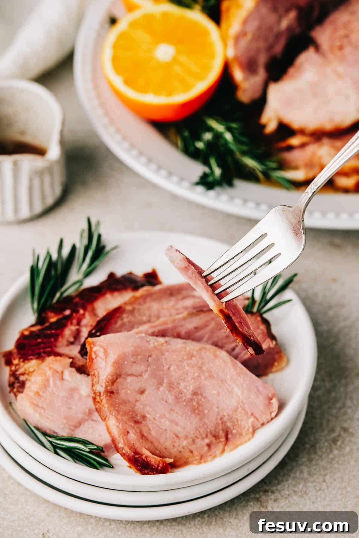A fork lifting a slice of ham from a small plate.