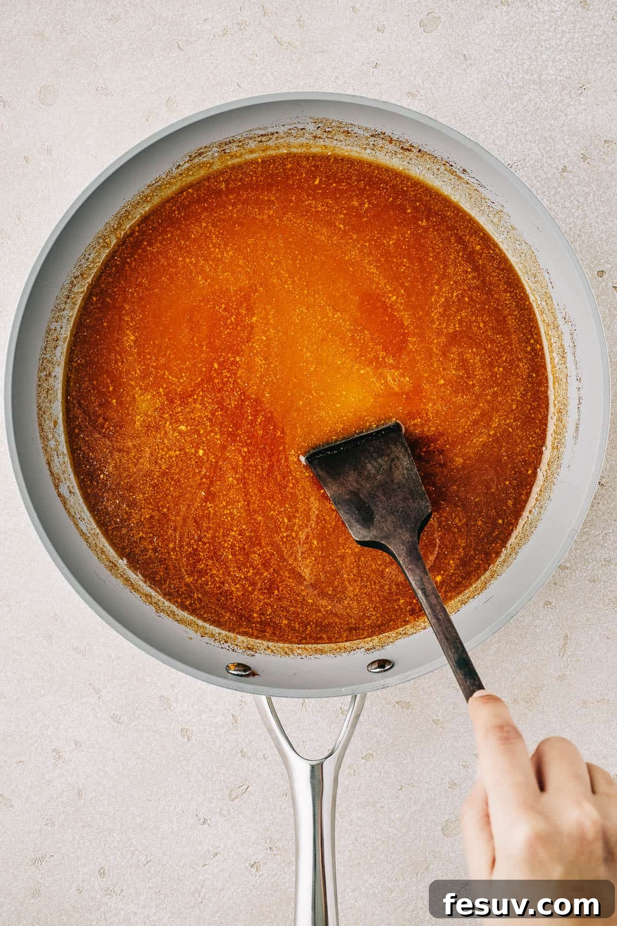 Ham glaze in a saucepan. A woman is stirring the glaze with a spatula.