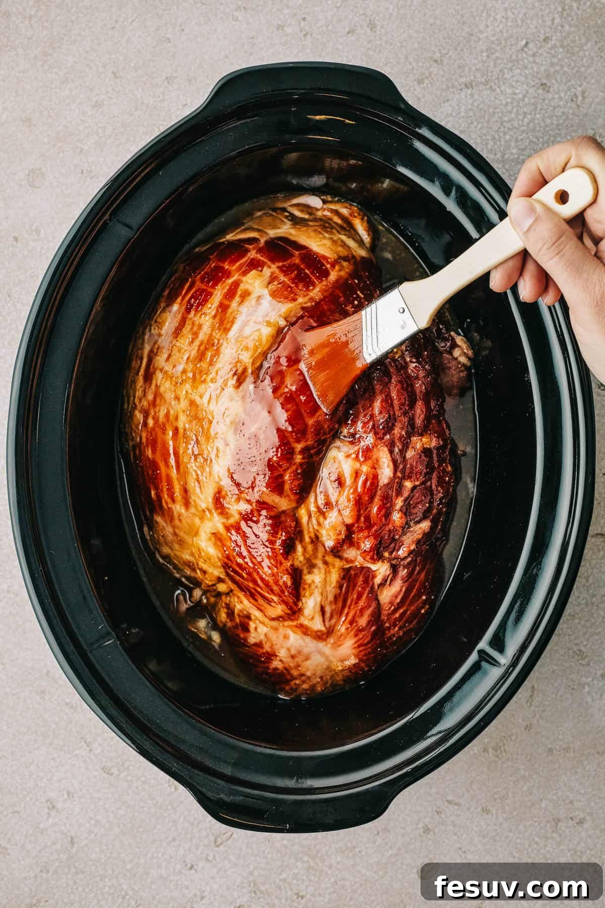 Overhead shot of a ham in a crockpot insert, being brushed with glaze.