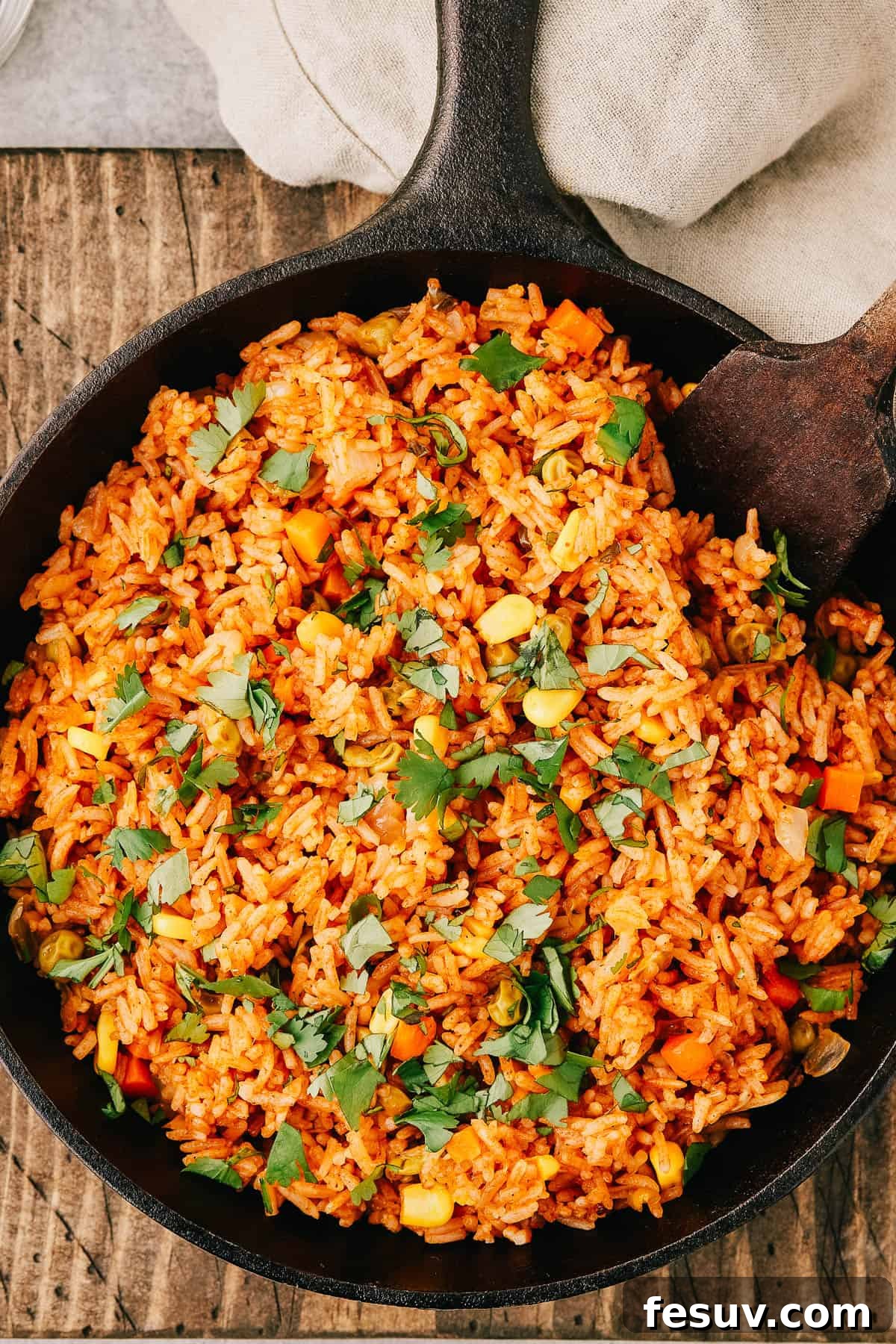 Overhead shot of a pan of spanish rice with a wooden utensil in the pan, garnished with fresh cilantro and a lime wedge.