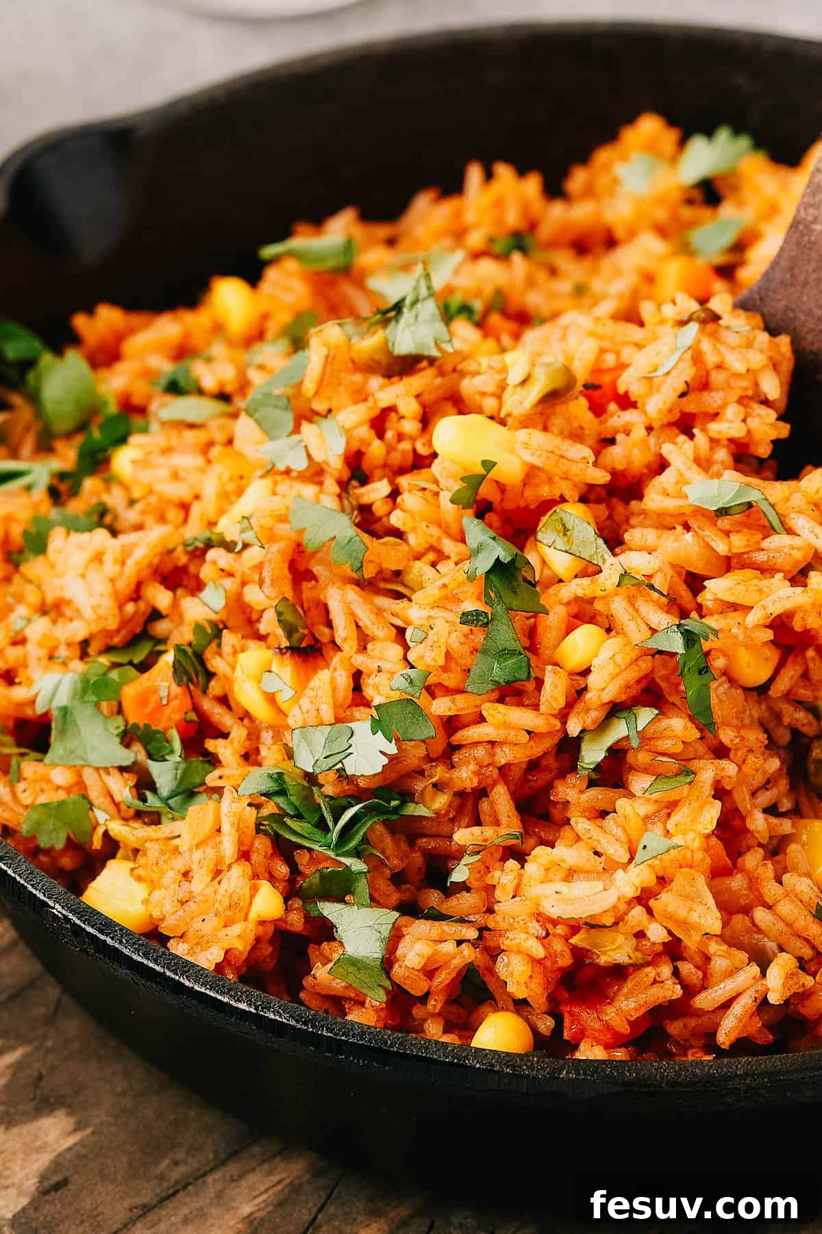 Side view of a serving of Instant Pot Mexican rice in a cast iron skillet, with a wooden serving spoon.