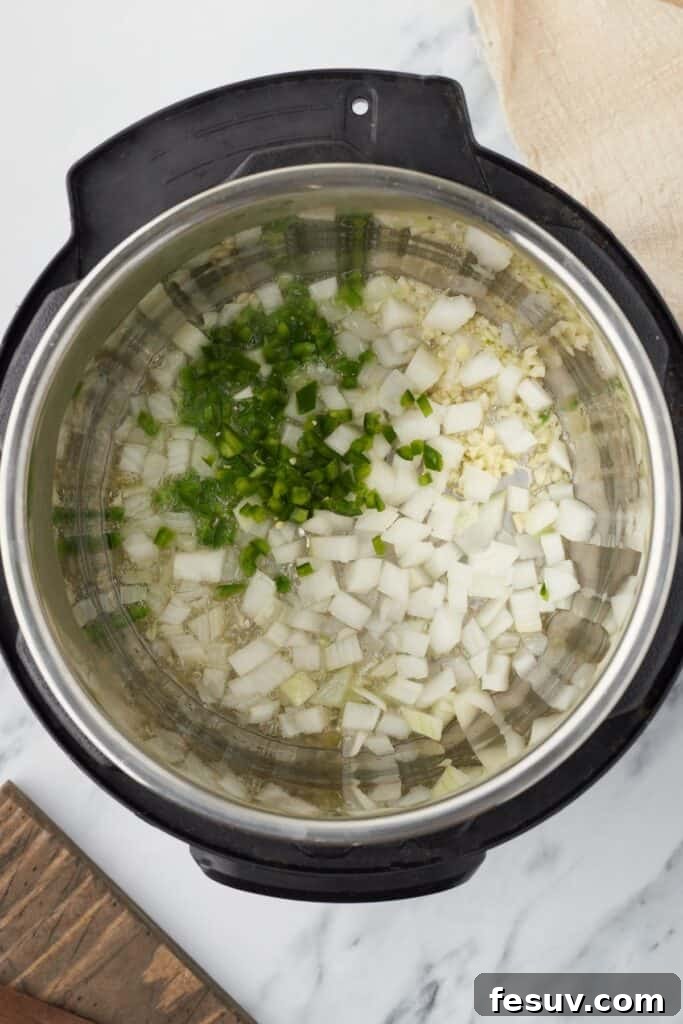 Overhead shot of an Instant Pot, with diced onions, minced garlic, and minced jalapeno inside, beginning to saute.