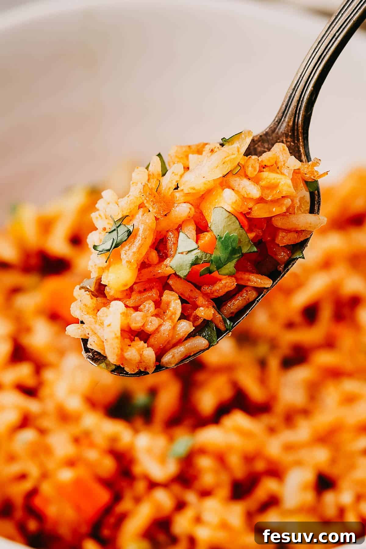 A spoon lifting a perfect bite of fluffy Instant Pot Mexican rice out of a white bowl, showcasing the vibrant colors of the vegetables.