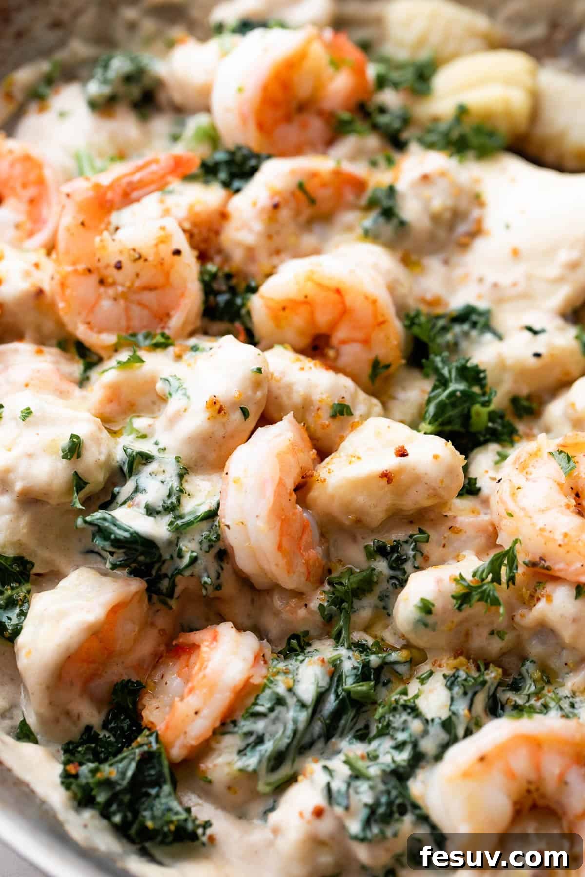 Velvet Parmesan Gnocchi with Succulent Shrimp 3 up close shot of a steel skillet filled with cream sauce, gnocchi, shrimp, and greens.