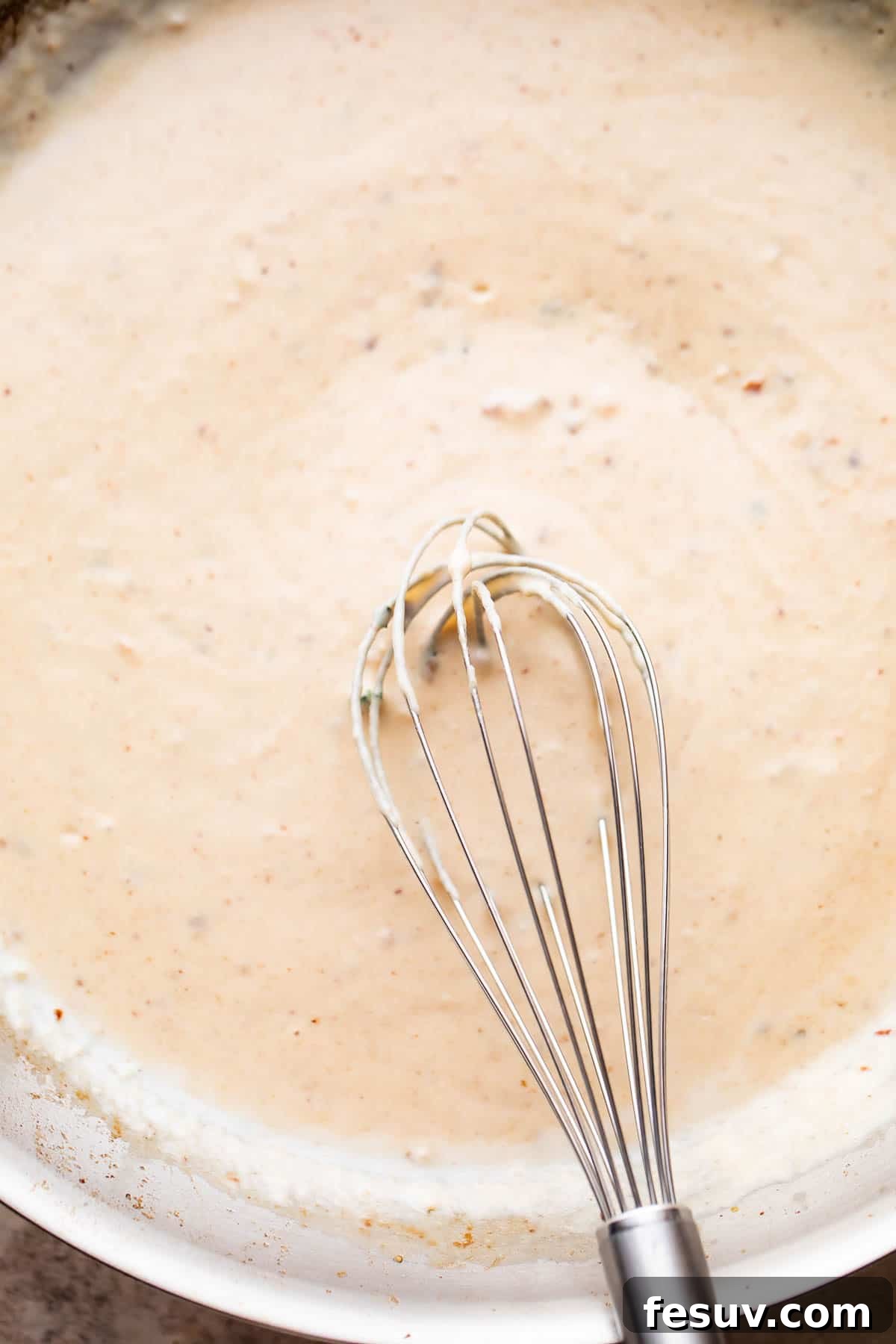 Velvet Parmesan Gnocchi with Succulent Shrimp 5 whisking through white cream sauce in a skillet.