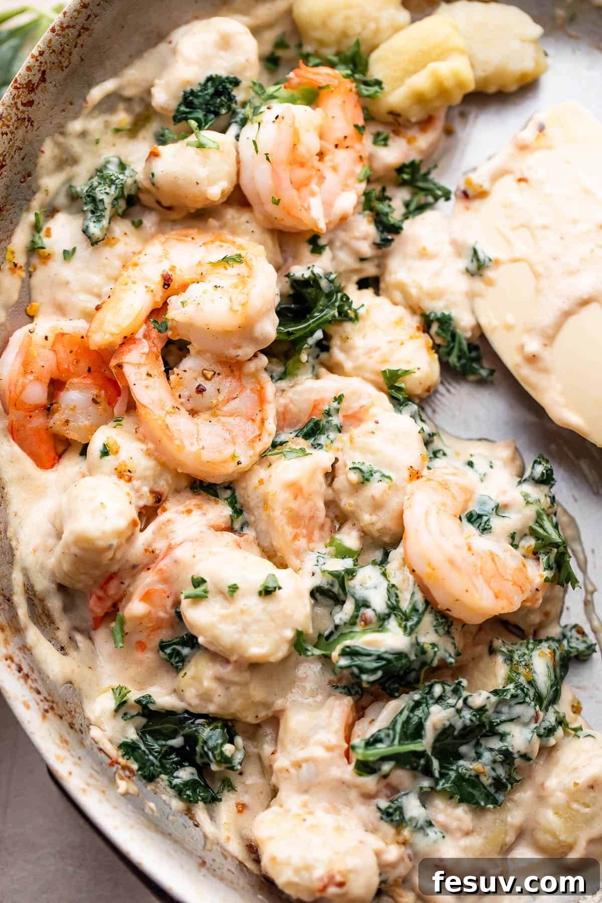 Velvet Parmesan Gnocchi with Succulent Shrimp 6 up close shot of a steel skillet filled with cream sauce, gnocchi, shrimp, and greens.
