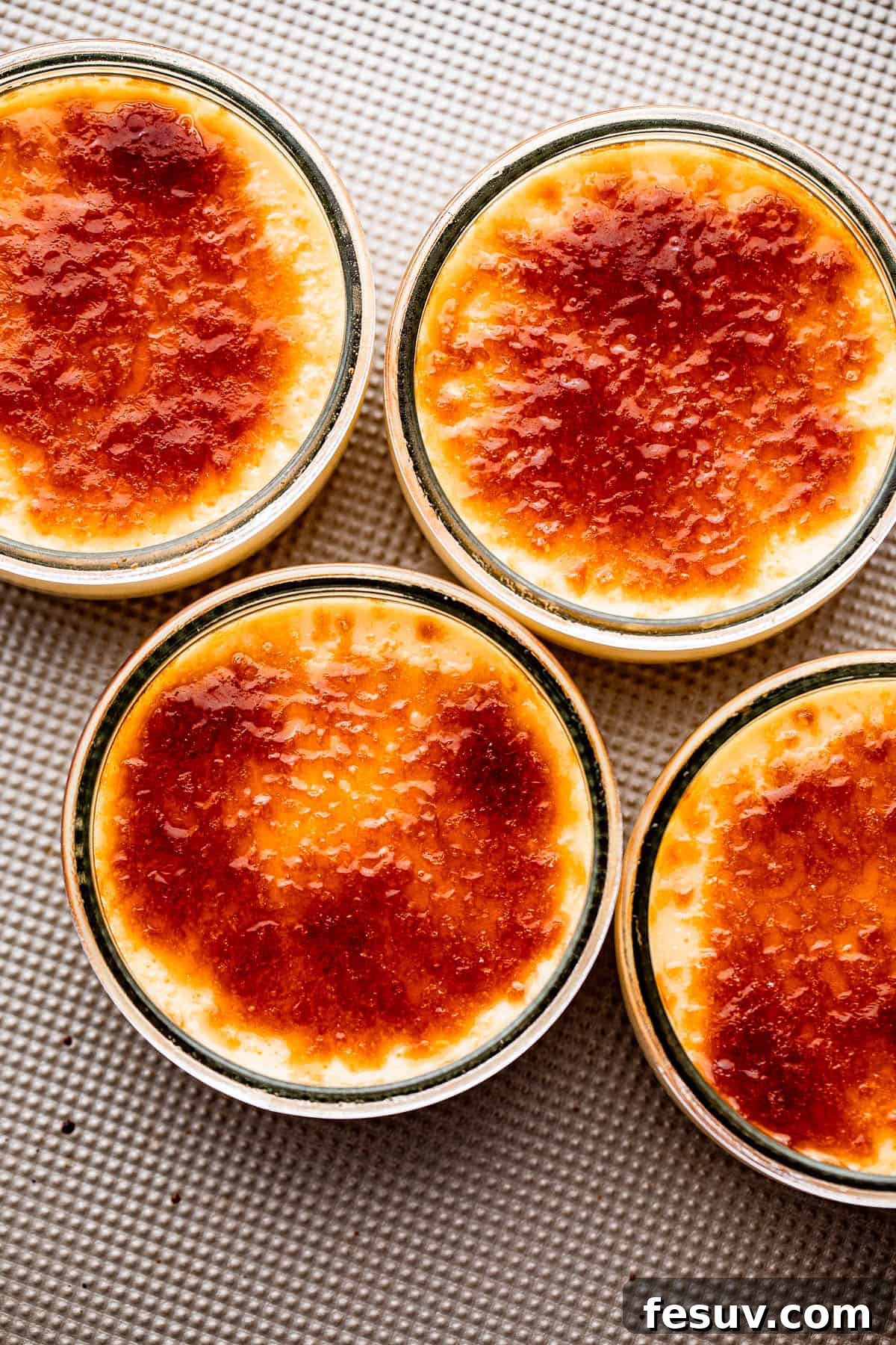 Overhead shot of four small ramekins filled with uncooked creme brulee custard, arranged on a metallic surface.