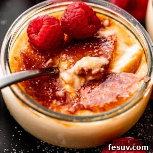 Side shot of Creme Brulee in a glass jar, topped with two raspberries, and a spoon inside the jar.