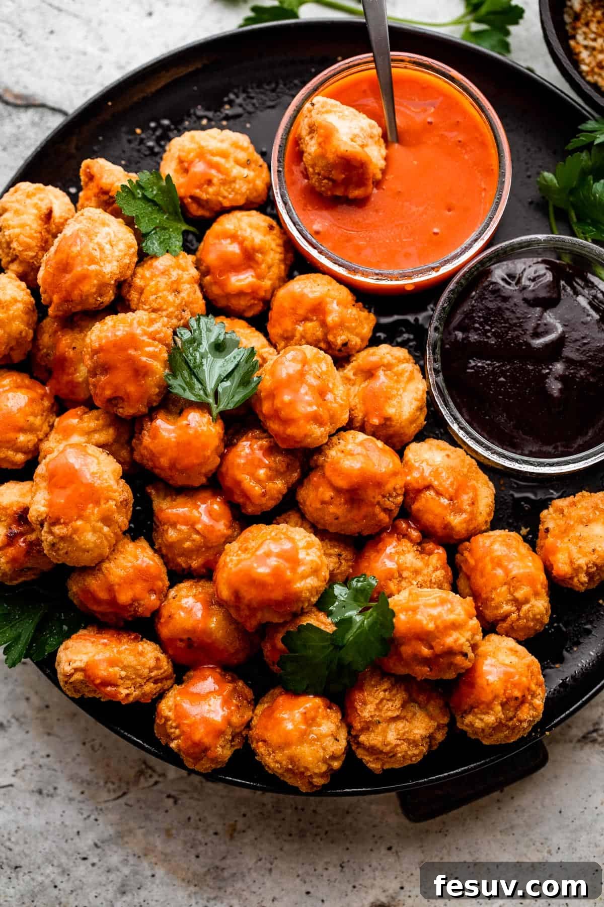 overhead shot of popcorn chicken arranged on a black plate with bowls of buffalo sauce and barbecue sauce placed right next to it.