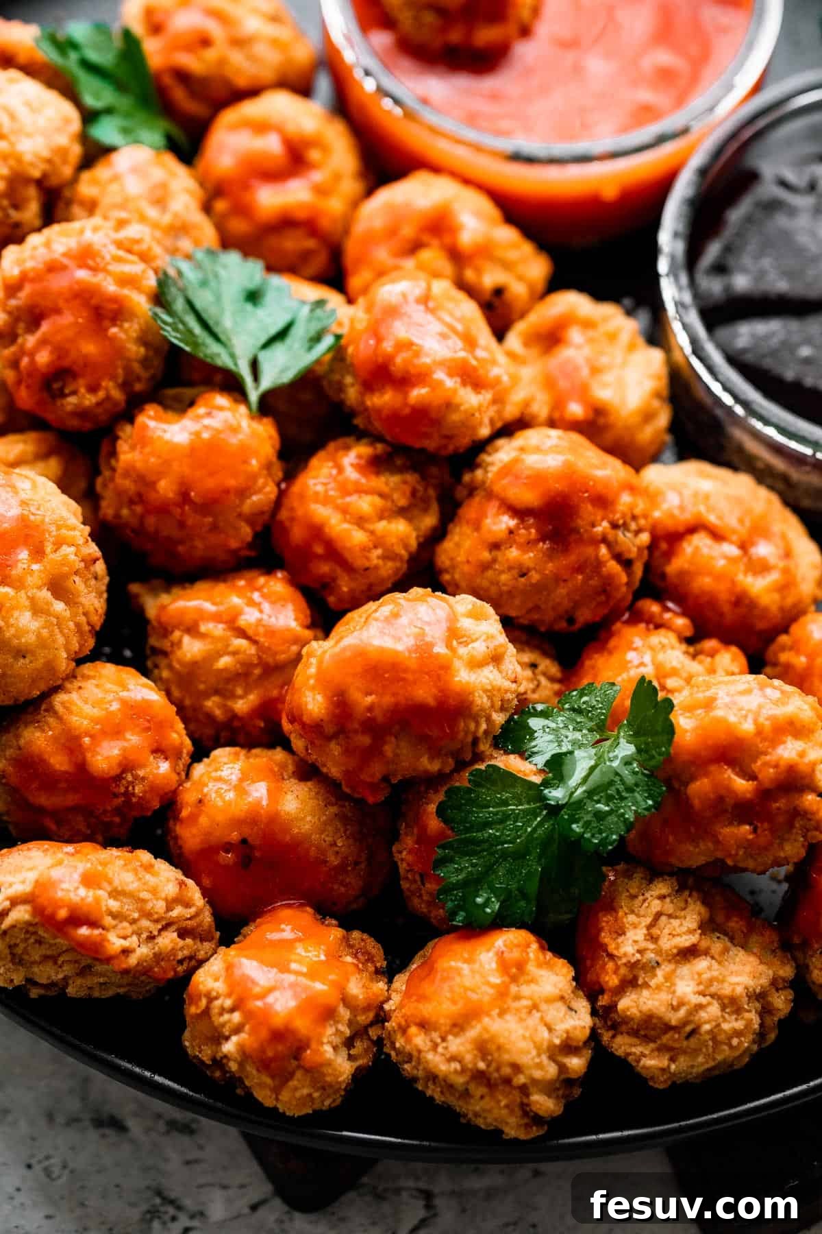 overhead shot of popcorn chicken arranged on a black plate with bowls of buffalo sauce and barbecue sauce placed right next to it.