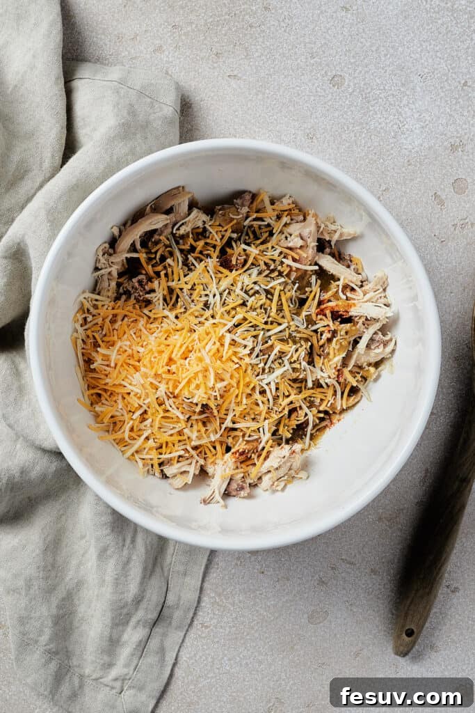 Smothered Green Chili Chicken Enchiladas 5 A white mixing bowl brimming with the prepared chicken enchilada filling, showing shredded chicken, melted cheese, and green spices perfectly blended.
