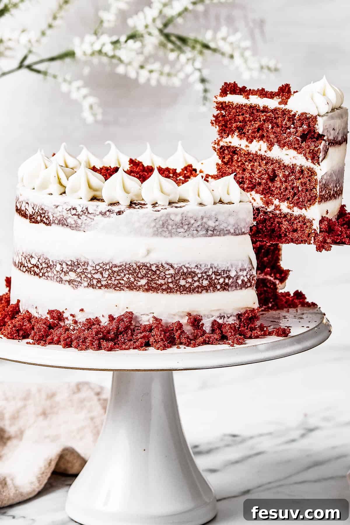 A woman's hand gracefully lifts a slice of red velvet cake, emphasizing its perfect layers and generous frosting.