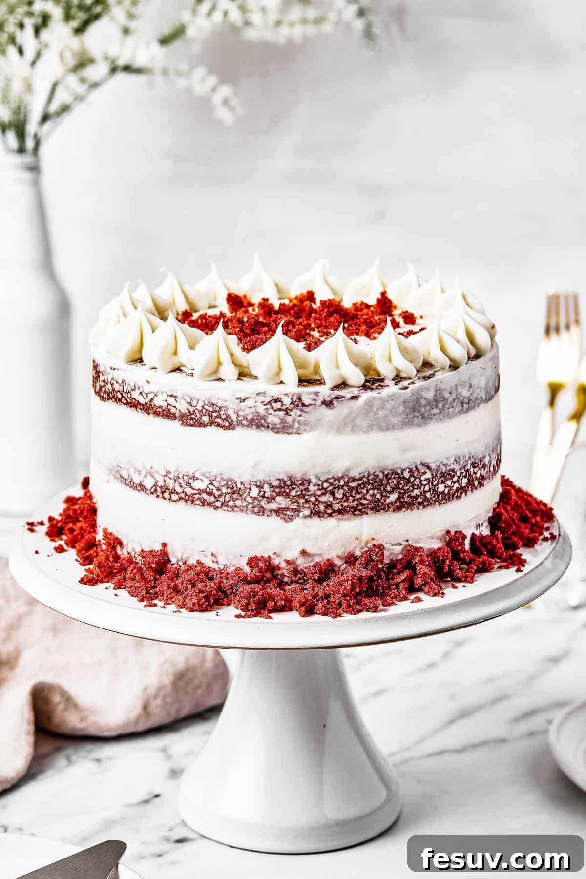 A beautifully frosted red velvet cake sits on an elegant cake stand, ready to be served.