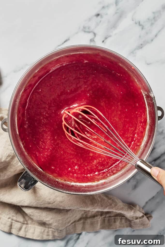 A large mixing bowl containing vibrant red cake batter with a whisk resting in it, showing its smooth consistency.