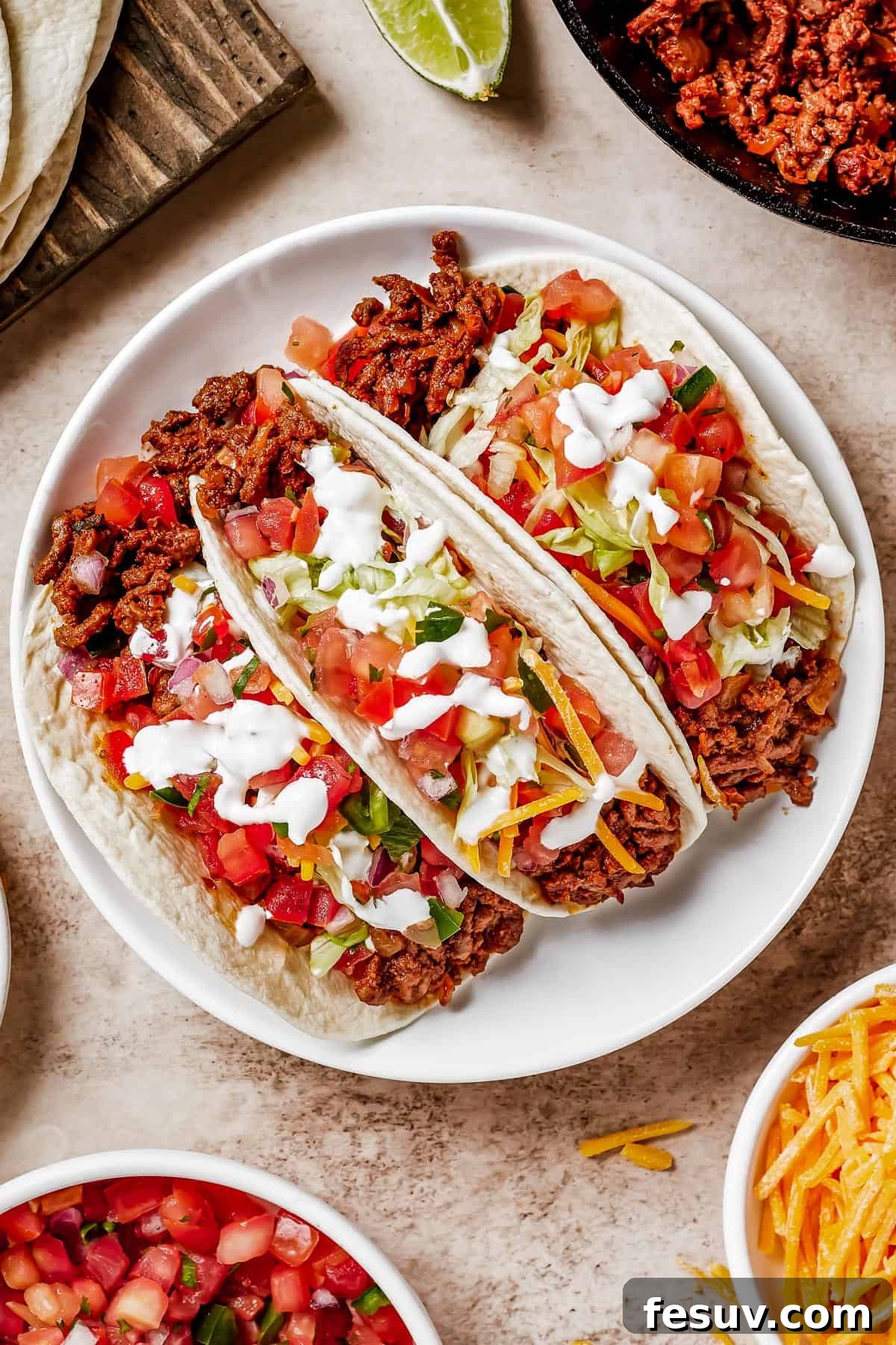 Three soft tacos on a plate with lime wedges.