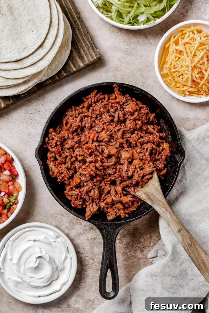 wooden spoon stirring through a skillet full of cooked meat for tacos.