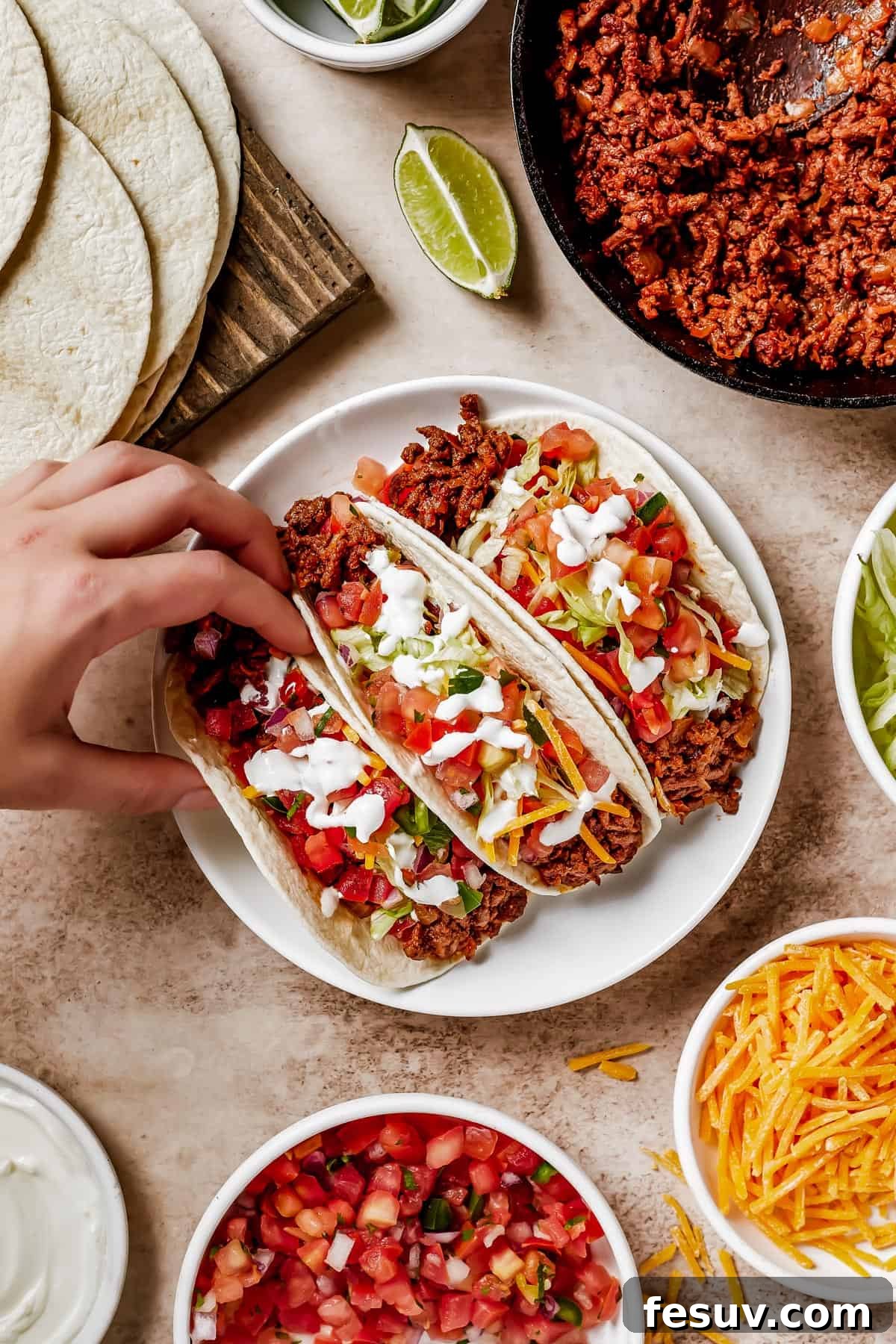 A woman's hand lifts a soft taco off of a plate.