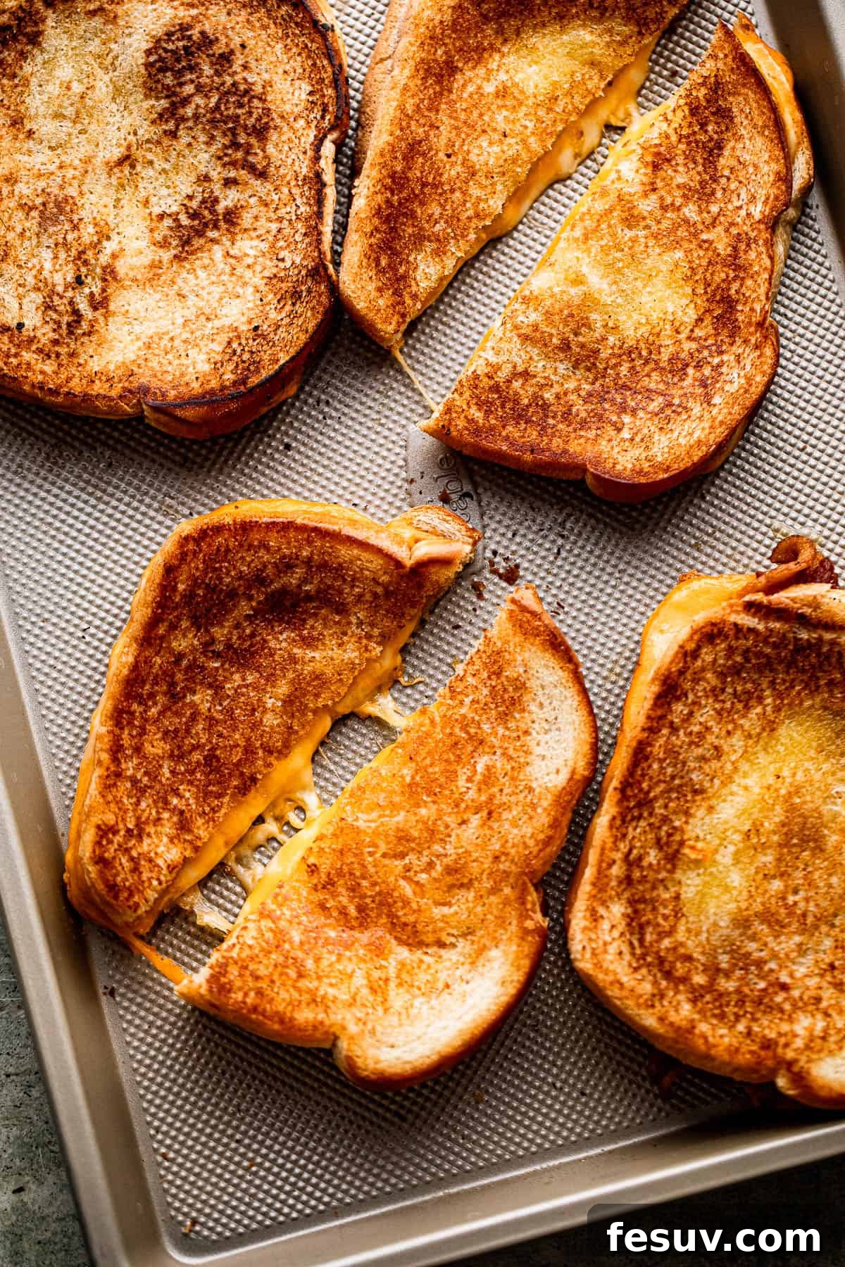 Sheet Pan Grilled Cheese Perfection 2 Four golden baked grilled cheese sandwiches, diagonally cut in half, arranged neatly on a baking sheet.