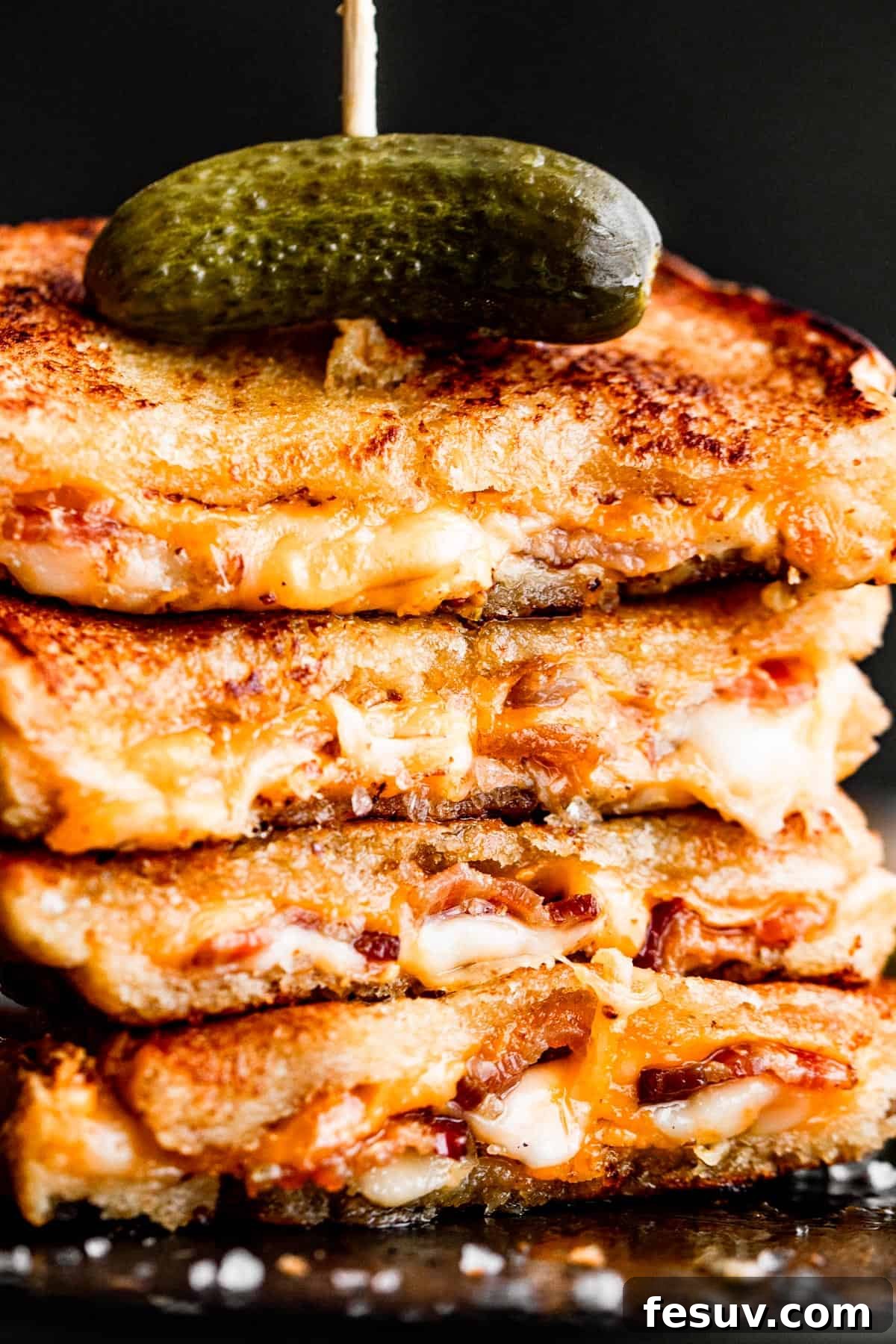 Sheet Pan Grilled Cheese Perfection 3 A stack of golden grilled cheese sandwiches, speared with a long toothpick and topped with a pickle slice, ready to be served.