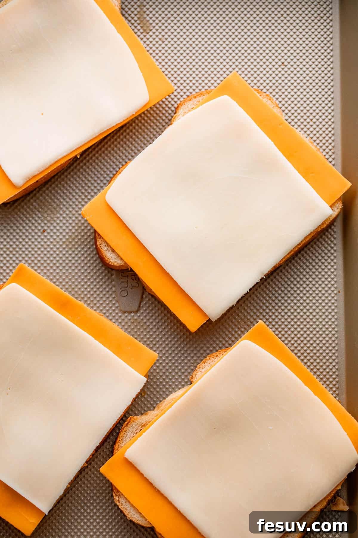 Sheet Pan Grilled Cheese Perfection 5 Eight slices of cheese meticulously placed on four slices of bread, forming the base for delicious baked grilled cheese sandwiches.