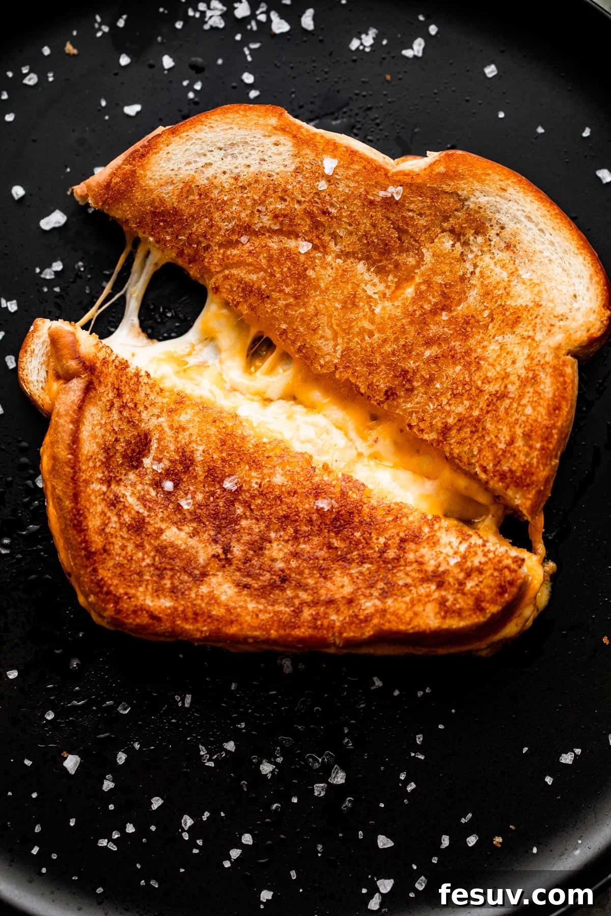 Sheet Pan Grilled Cheese Perfection 6 A baked grilled cheese sandwich, cut in half, with luscious melted cheese stretching invitingly from the center.