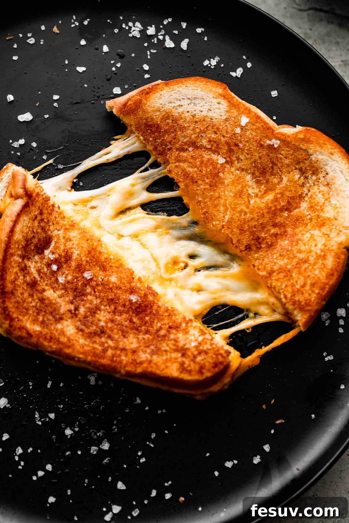 Sheet Pan Grilled Cheese Perfection 7 Another mouth-watering shot of a baked grilled cheese sandwich, split open to reveal copious amounts of melted, stringy cheese.