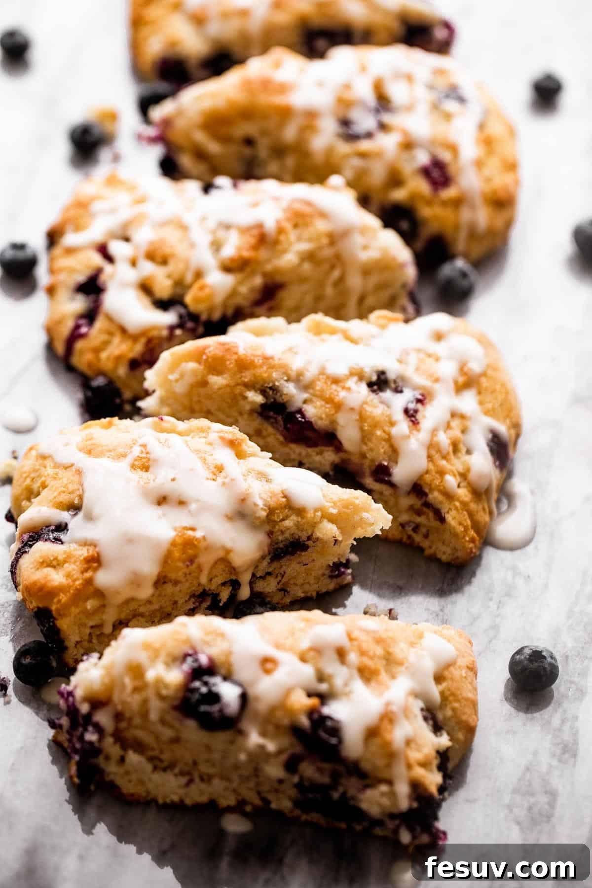 Six glazed blueberry scones on a marble board. six blueberry scones arranged in a single row on a marble board