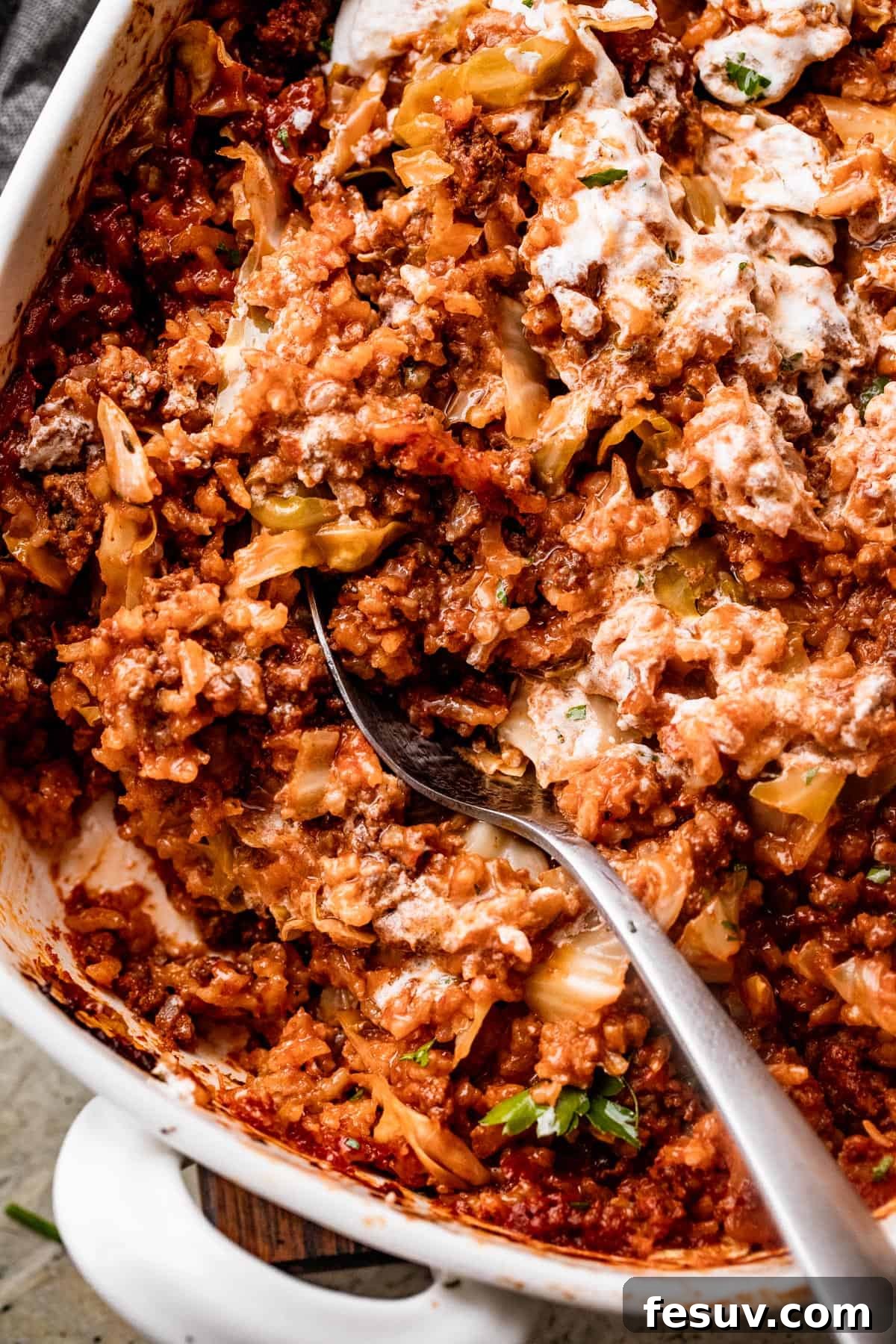Hearty Cabbage Roll Casserole 3 long spoon stirring through Cabbage Roll Casserole in a white baking dish.