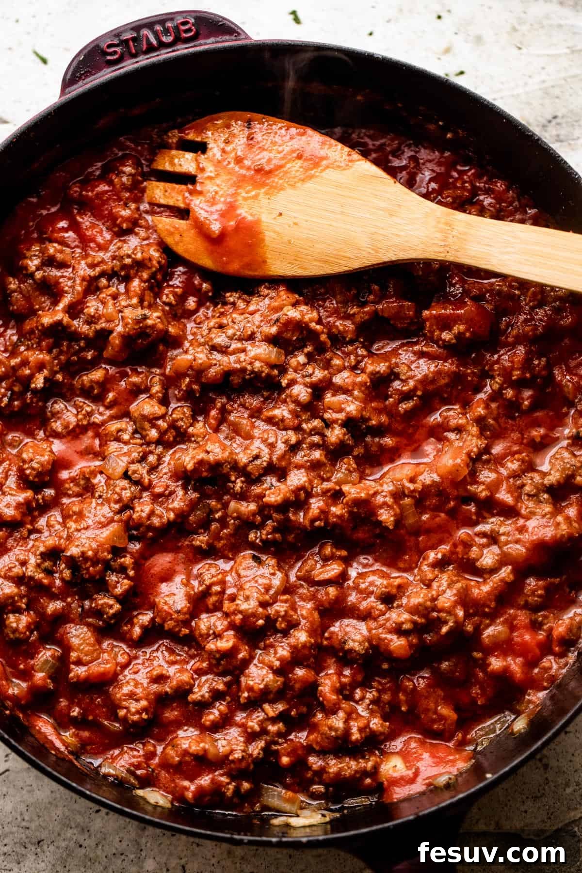 Hearty Cabbage Roll Casserole 5 wooden spoon stirring through ground beef that's cooking in a black skillet.