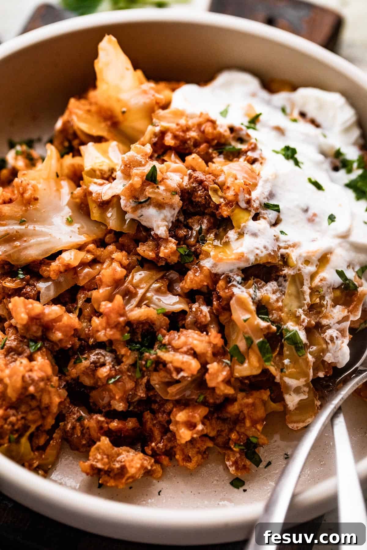 Hearty Cabbage Roll Casserole 8 Cabbage Roll Casserole served in a bowl, topped with sour cream, and two utensils placed inside the bowl.