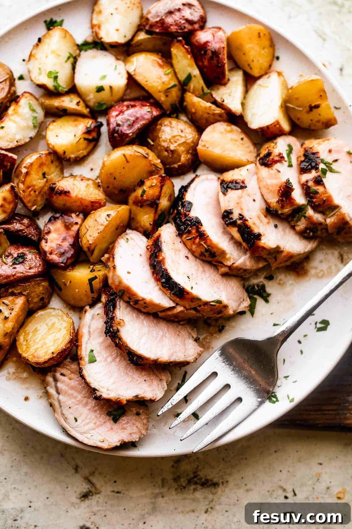 Herb-Crusted Pork Tenderloin with Golden Potatoes 2 Overhead shot of a serving plate with sliced roast pork tenderloin served with colored baby potatoes, garnished with fresh rosemary