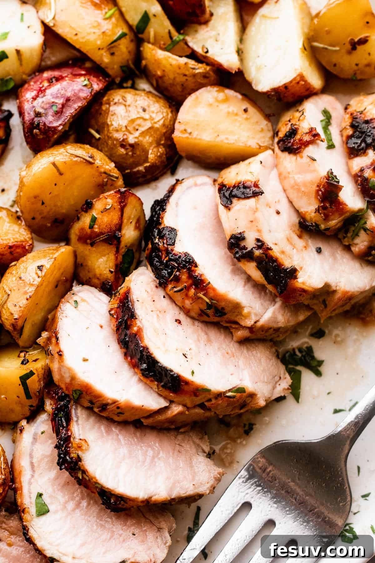 Herb-Crusted Pork Tenderloin with Golden Potatoes 3 Close-up shot of perfectly sliced roast pork tenderloin with crispy, seasoned baby potatoes