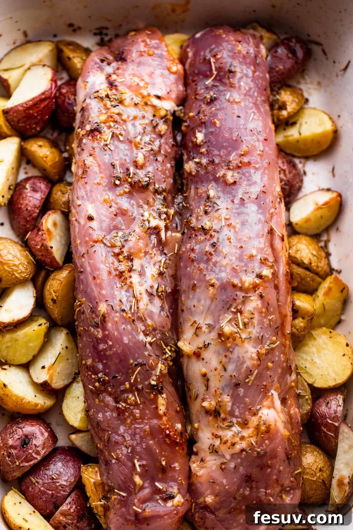 Herb-Crusted Pork Tenderloin with Golden Potatoes 5 Two raw pork tenderloins set over a bed of seasoned baby potatoes in a baking dish, before roasting