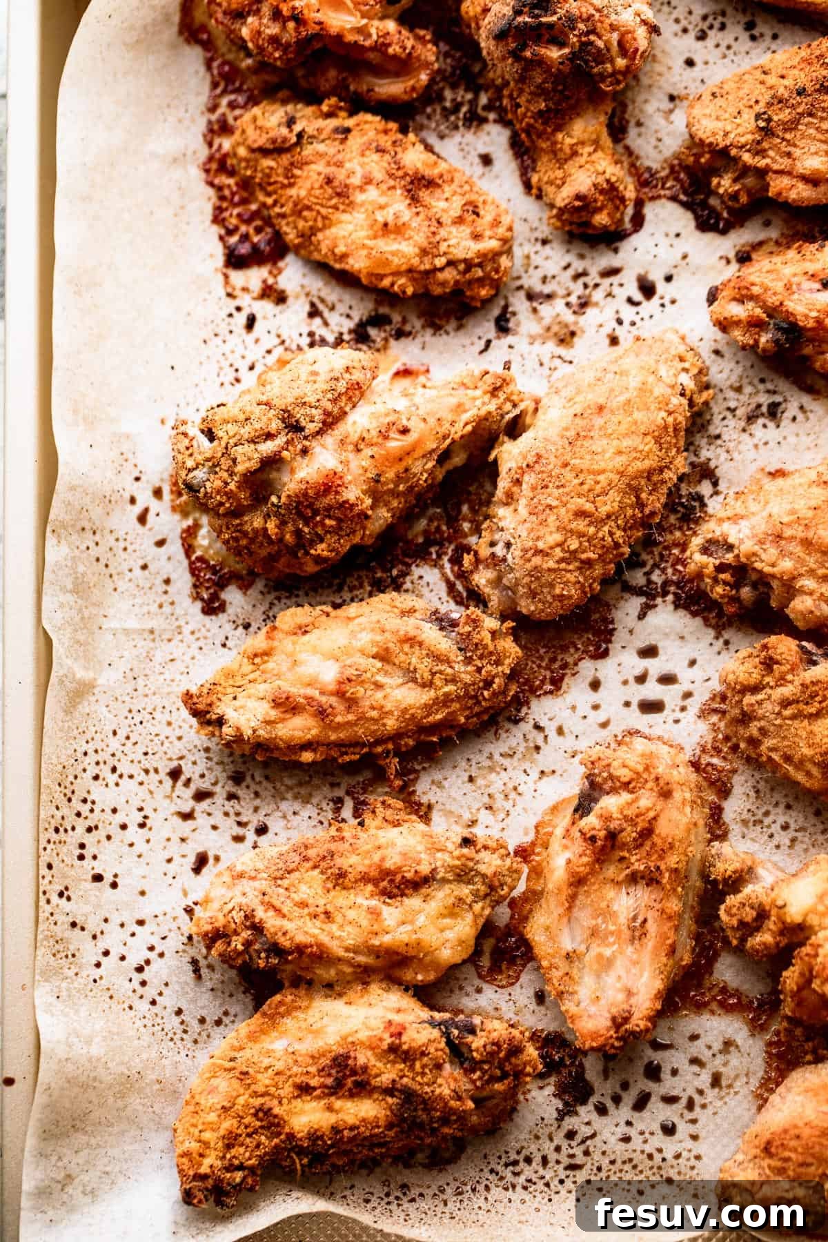 overhead shot of cooked hot wings arranged on a parchment lined baking sheet.