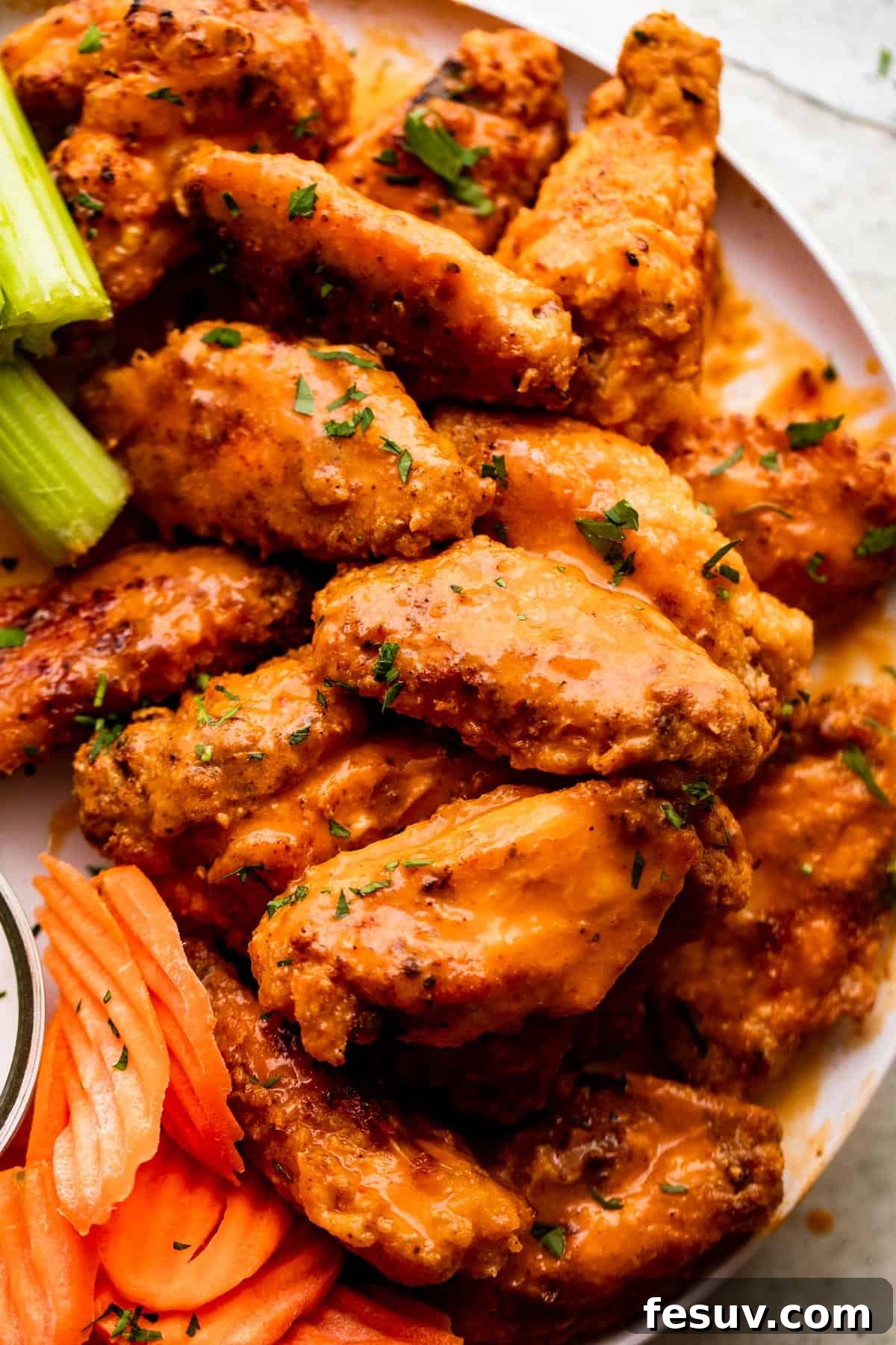 close up overhead shot of Mango Habanero Hot Wings arranged on a white serving plate with celery sticks and carrots set alongside the wings.