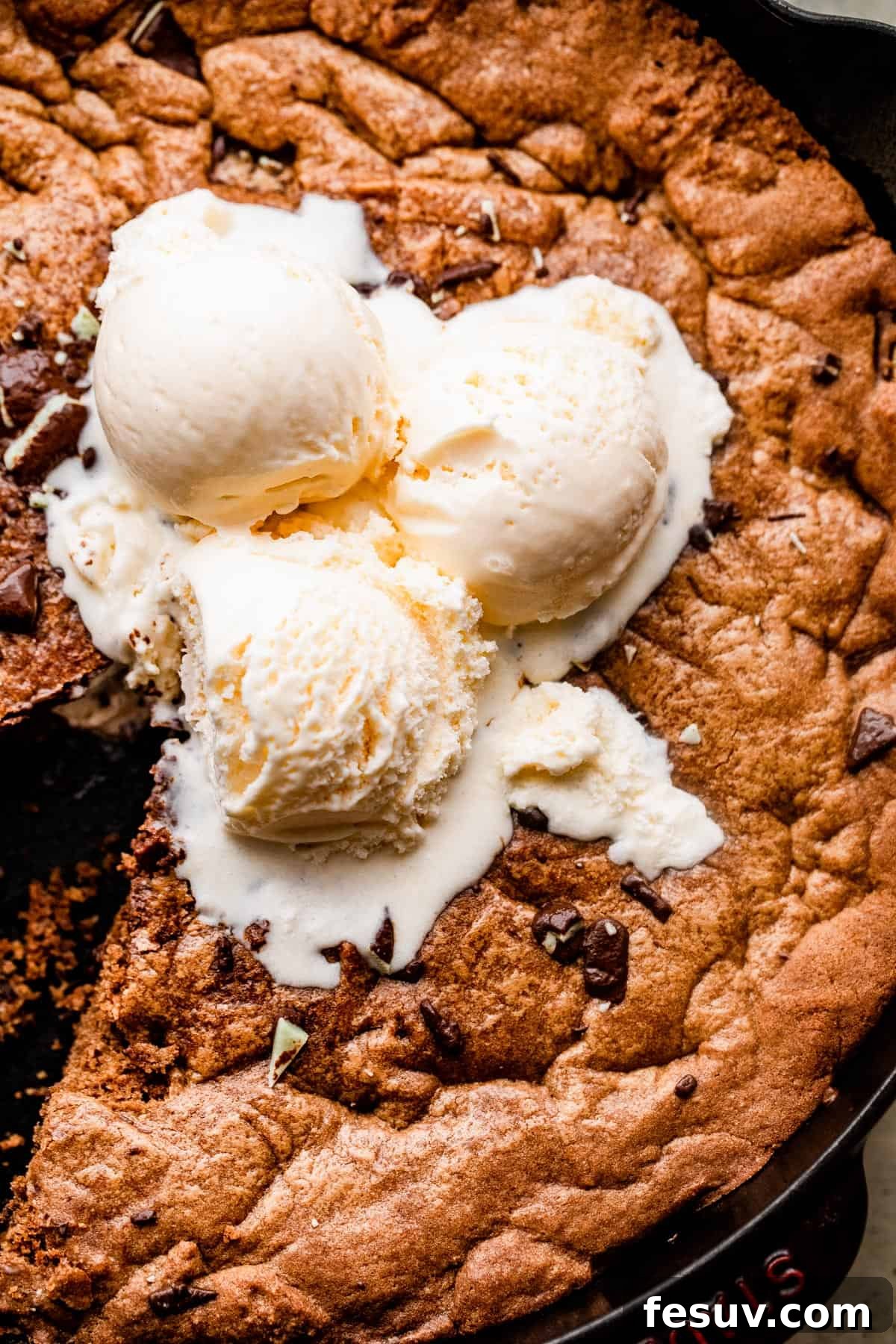 Close-up overhead shot of three scoops of vanilla ice cream melting on top of a large, warm mint chocolate skillet cookie, ready to be served.