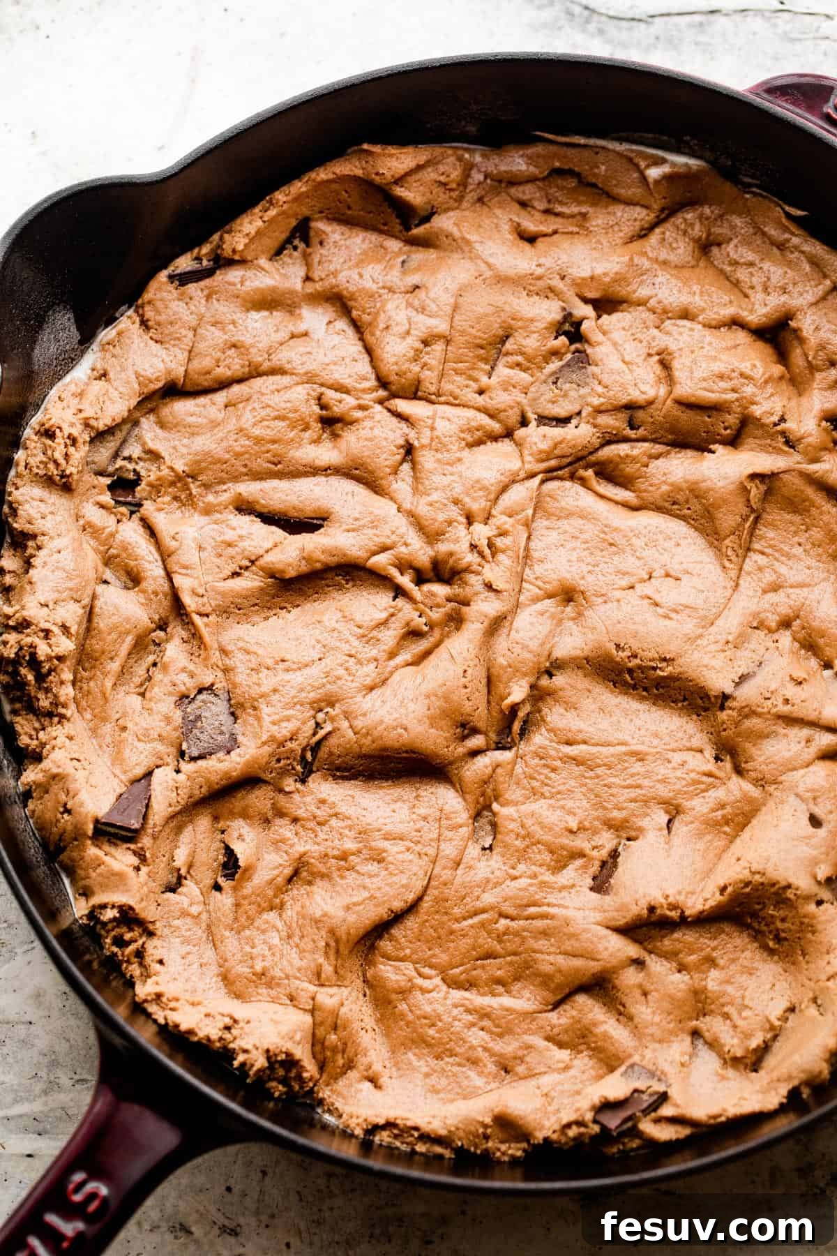 Raw, uncooked cookie dough, studded with mint chocolate pieces, spread evenly into a cast iron skillet, ready for baking.