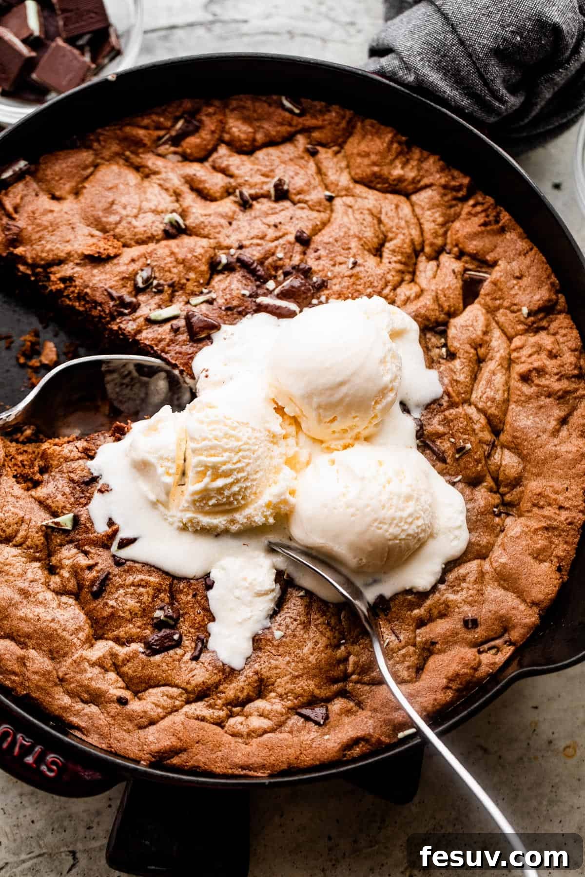 Overhead shot of a warm mint chocolate skillet cookie served directly in the cast iron skillet, adorned with three generous scoops of melting vanilla ice cream and two large spoons ready for sharing.