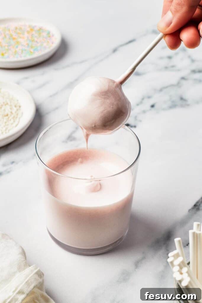 A ball of cake being dipped into a glass of melted candy coating.
