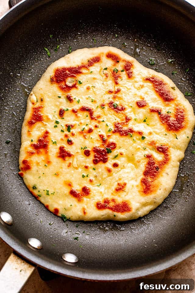 A golden-brown homemade flatbread cooking to perfection in a hot skillet, showing characteristic bubbles and slight charring.