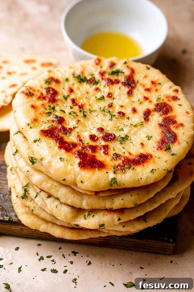 A close-up, inviting top view of a stack of golden homemade flatbreads on a wooden board, next to a small bowl of olive oil, ready to be served.